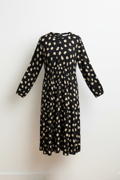 Schwarzes Kleid mit Punktmuster vor weißer Wand