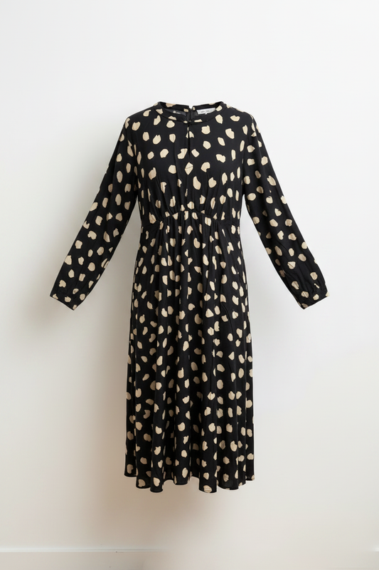 Schwarzes Kleid mit Punktmuster vor weißer Wand